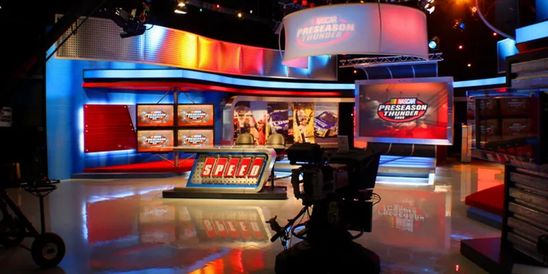 A broadcast television studio with monitor walls and a studio camera, photographed by Tom Atkins